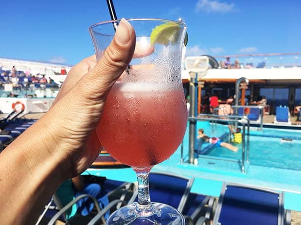 Hand holding up a pink margarita with the pool behind