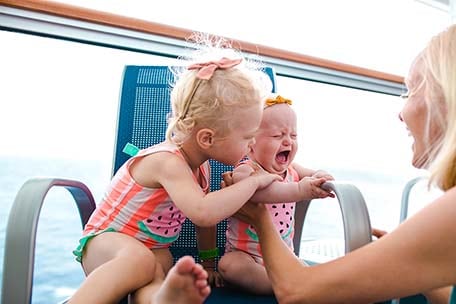 Two young girls sitting in a chair with their mom looking at them on Carnival Vista