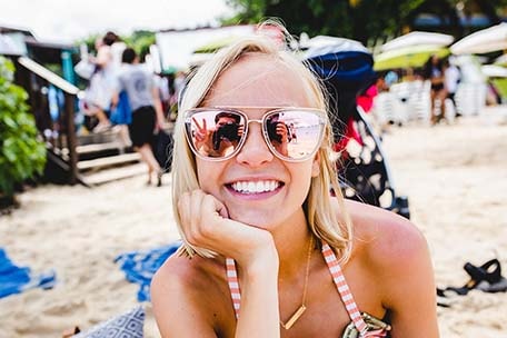 Close up of Hailey on a beach smiling in sunglasses