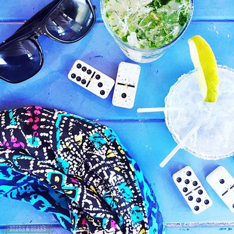 Overhead image of drinks, dominos and sunglasses sitting on a blue table