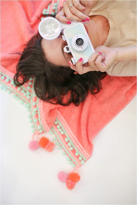 Woman laying down on towel holding a camera up to her face