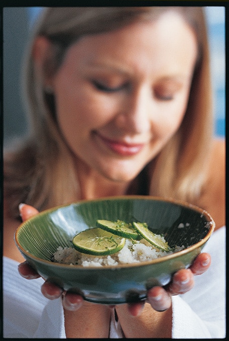 a woman holding a bowl of the ginger and lime body scrub