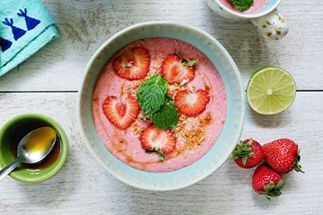 Strawberry coconut soup garnished with mint leaves, toasted coconut, strawberry slices and coconut nectar