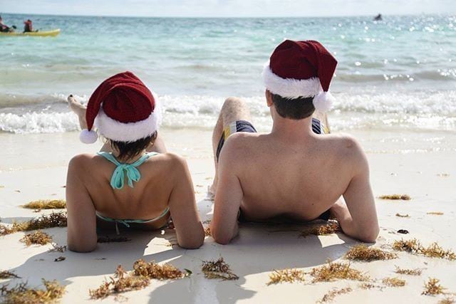 a man and a woman lying on a beach wearing santa hats