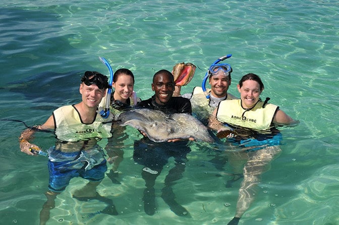 people standing in the ocean around a trainer holding a stingray in stingray cove