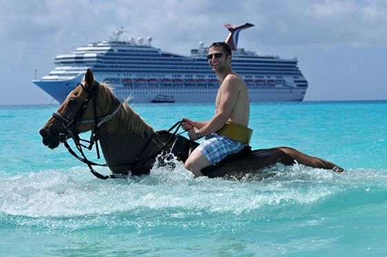 man riding a horse in the ocean shore with carnival cruise ship in the background