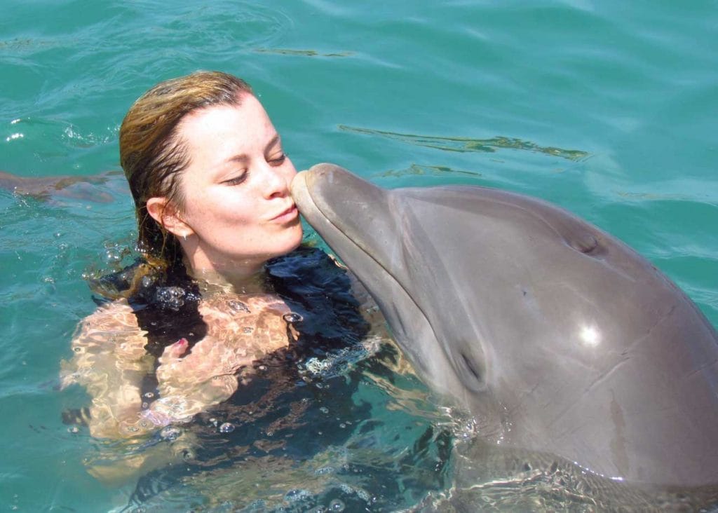 woman kissing a dolphin as they swim in dolphin cove