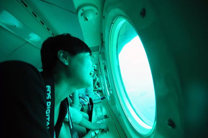 man laughing as he stares out of a window inside of a passenger submarine off the shore of barbados