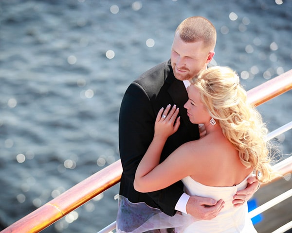 newlyweds holding each other as they stare out at the ocean onboard a cruise