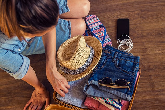 woman packing shorts, shirts, sunglasses and straw hat for vacation