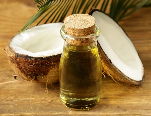 coconut oil in a glass jar in front of a freshly split coconut