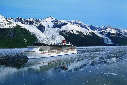 carnival ship cruising through alaska with snow filled mountains in the background