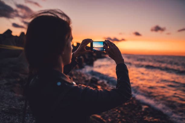 Woman on beach holiday taking photos with smartphone on sunset