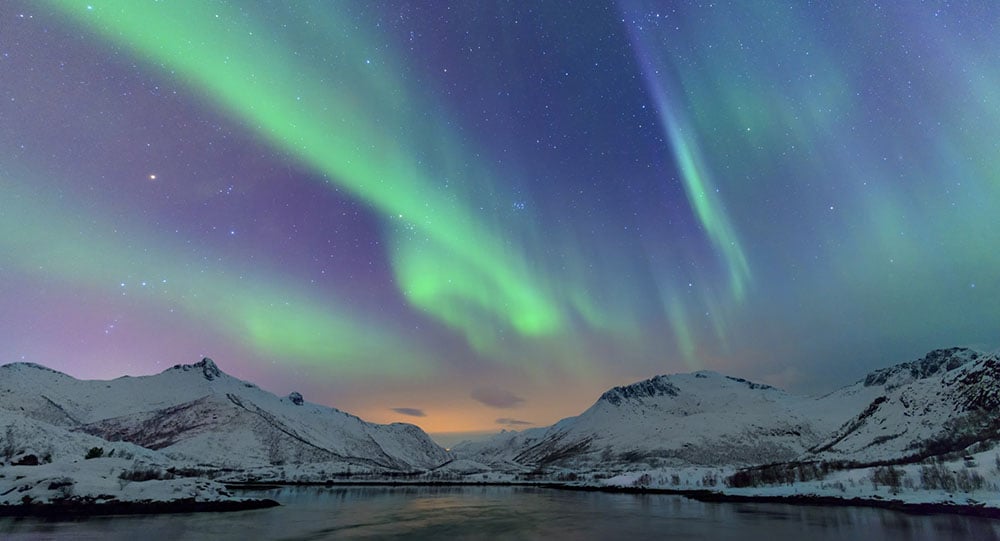 northern lights in the night sky with snowcapped mountains in the background