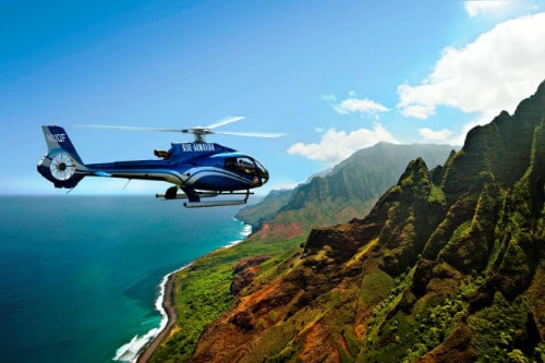 blue helicopter flying over the lush green mountains of hawaii