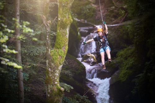 woman zip lining past a waterfall in the tropical forest of puerto vallarta