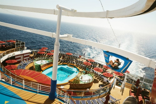aerial view of a woman riding a blue skyride over the pool of a carnival ship 
