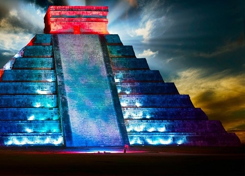 el castillo in chichen itza illuminated in a variety of different colors during the evening 
