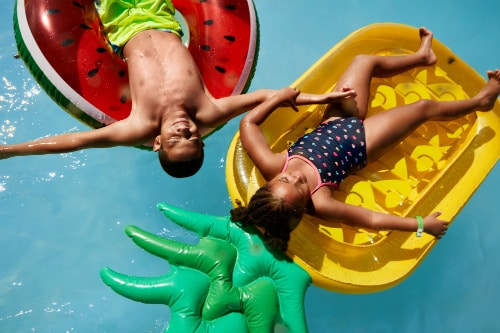 2 kids laying on an inflatable pineapple and watermelon float during a cruise