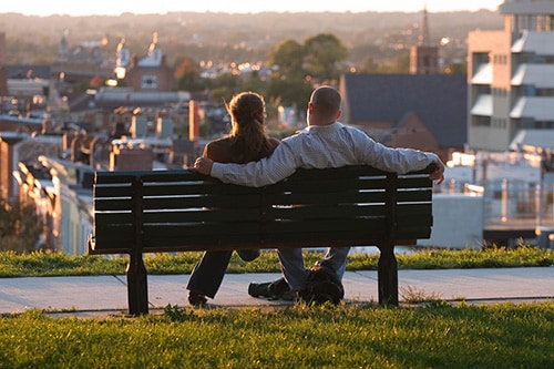couple sitting on a bench in federal hill park looking over baltmore suburbs 