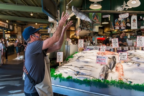 man tossing fresh fish in the local farmers market in the pike market neighborhood