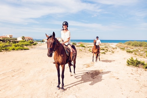 woman horseback riding along the beach in half moon cay as her husband follows