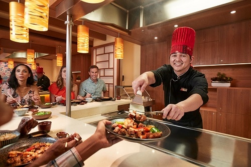 a chef serving fresh cooked food to a guest at bonsai teppanyaki onboard a carnival ship