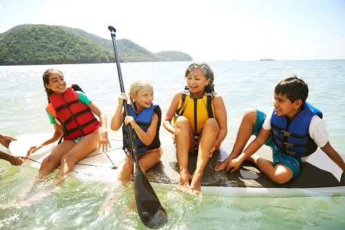a grandmother paddleboarding with her grandchildren