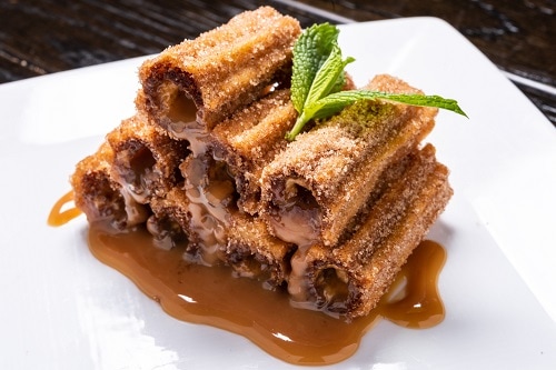 a plate of churros with cajeta and a mint for garnish