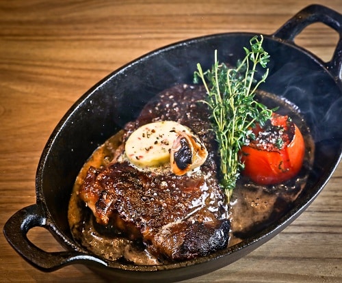 a steaming dish of steak, with parsley and tomato as a garnish