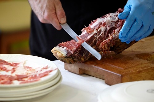 a server slicing up pieces of jamon iberico