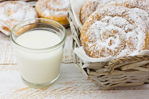 four swirl-shaped pastries dusted with powdered sugar called ensaimada with glass of milk