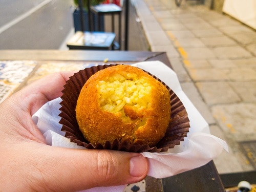 a tourist taking a bite of an arancine on the street