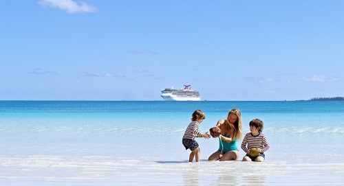 mother and children play in the sand while carnival ship sails in the background