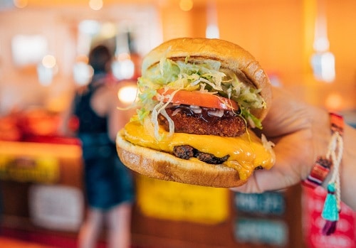 someone holding a burger with guy’s burger joint in the background