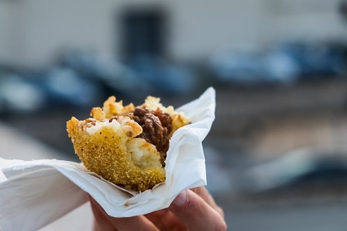 someone holding an arancini, a typical sicilian street food