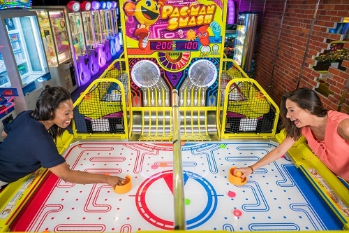 two women playing air hockey in the arcade onboard a carnival ship