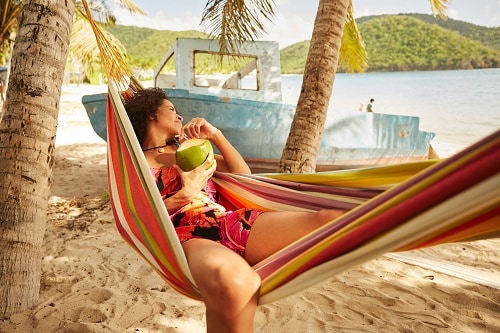 woman lounging on a hammock and drinking out of a coconut in the caribbean