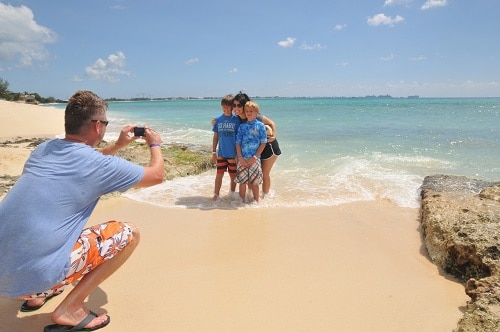 a dad taking a picture of his family on a grand cayman beach