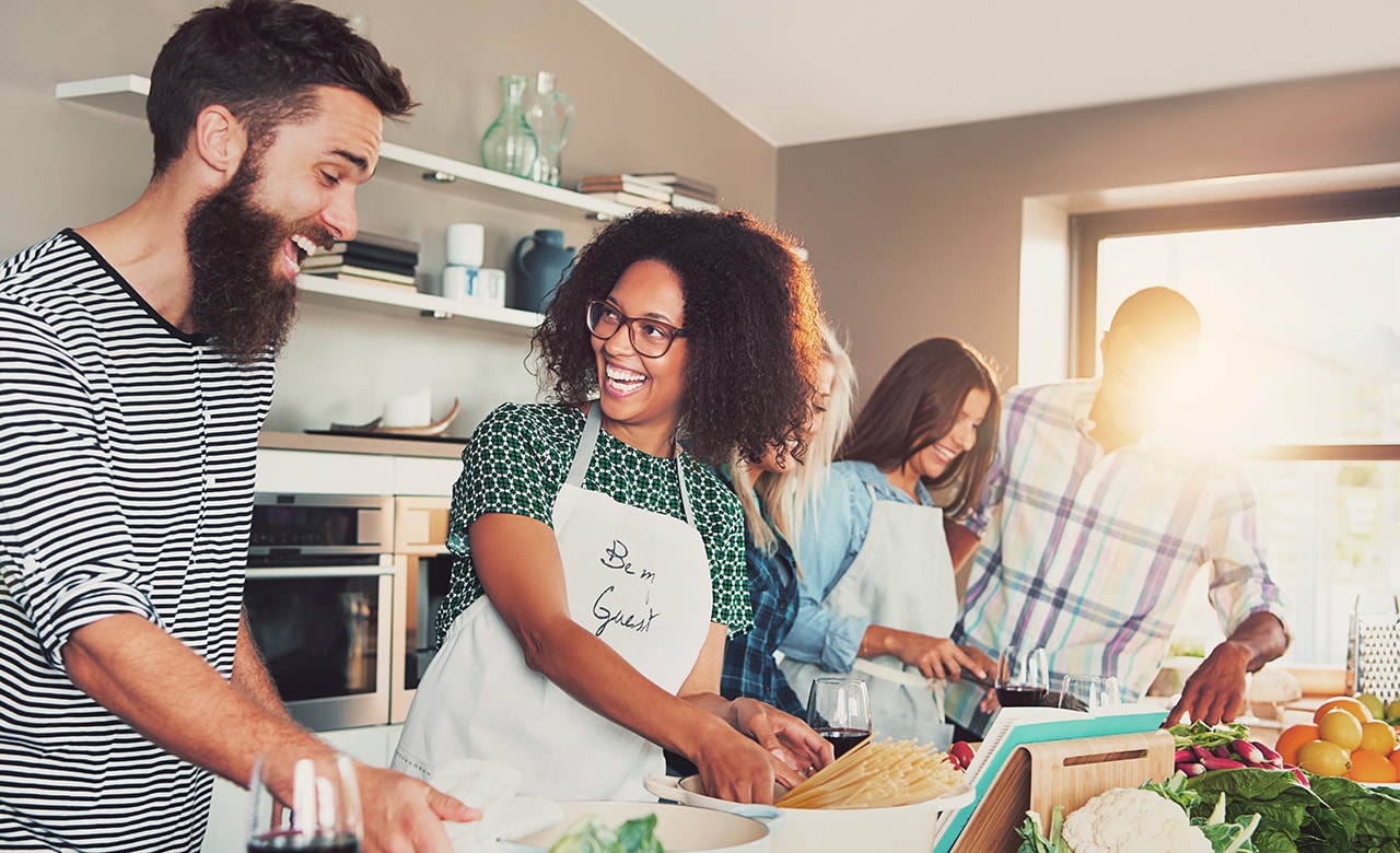 Laughing group of young cooking students in kitchen with bright sunlight pouring through window