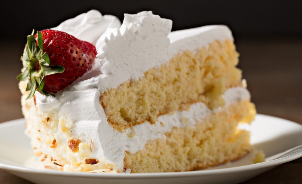 Slice of tres leches cake with a strawberry on top.