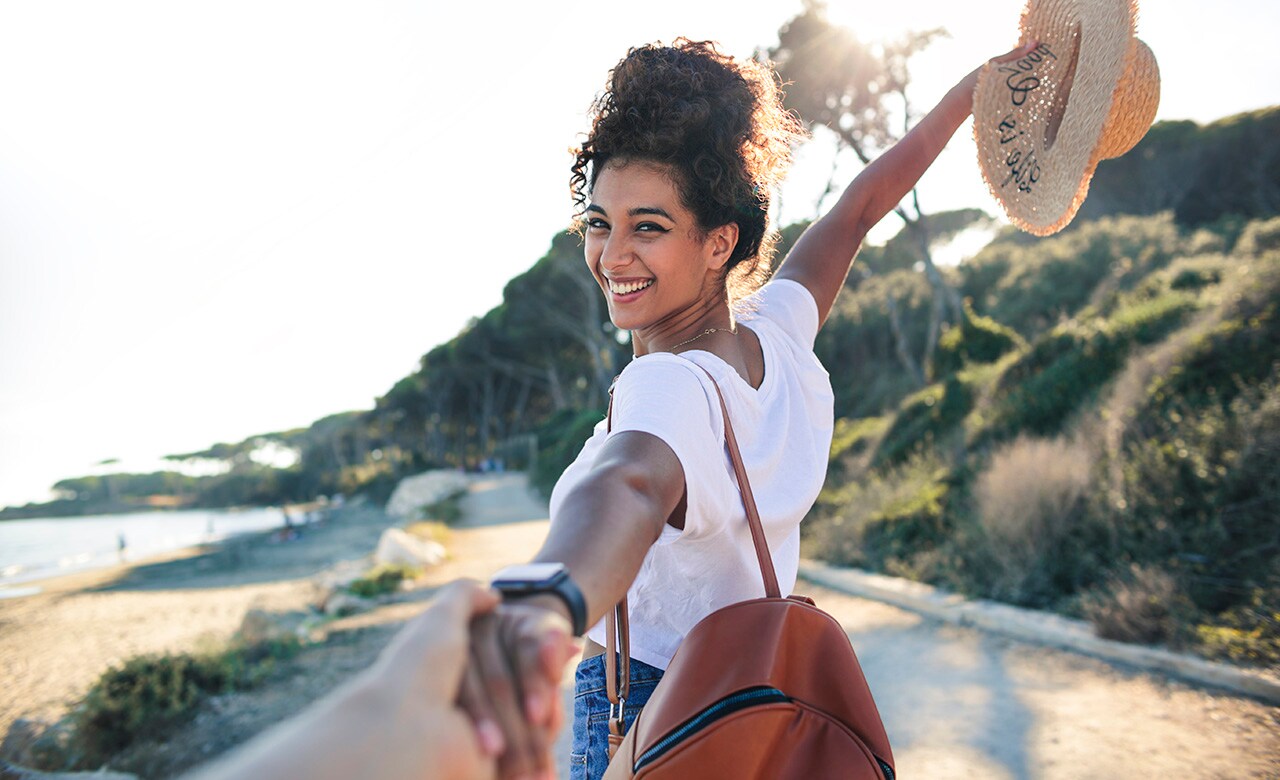 Young woman enjoying her vacation at the sea -Woman walking on a path by the beach, holding a friend's hand - Concept of freedom enjoyment