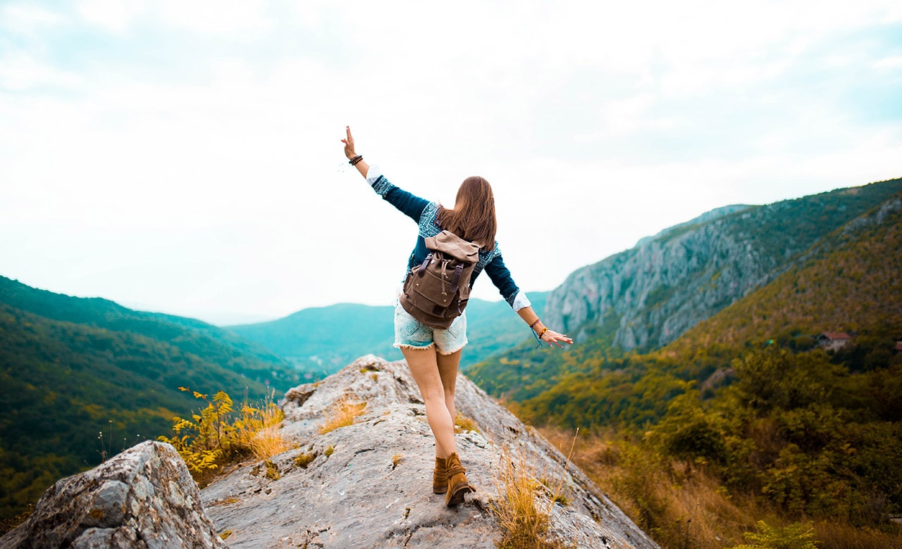 Young Hippie girl taking a walk on top of a mountain and enjoying the day. rear view