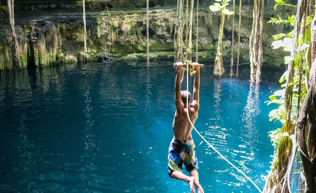 Young man using rope swing into cenote in Mexico