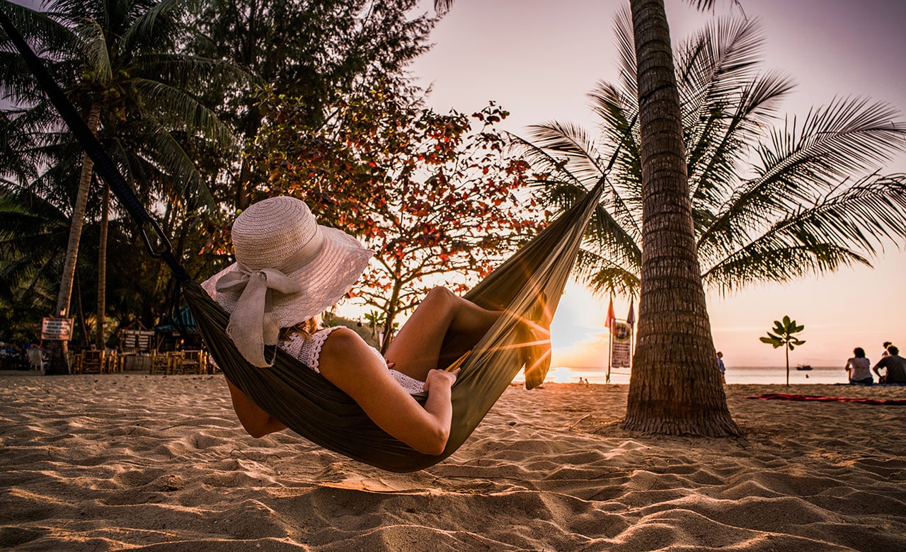 Woman relaxing in a hammock on a beach at sunset