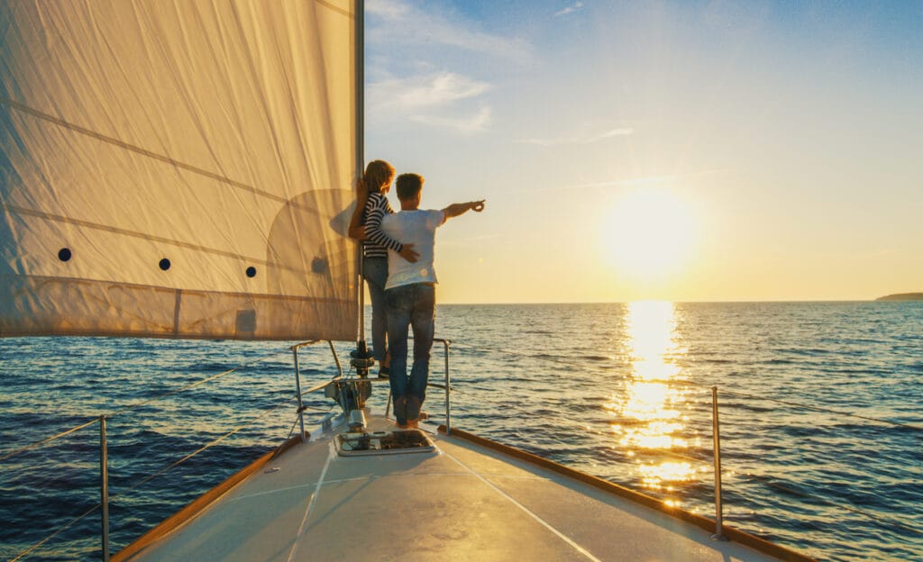 A couple sailing on the water and pointing to a setting sun