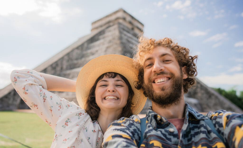 Couple taking a selfie in front of the Chichen Itza pyramid in Mexico.