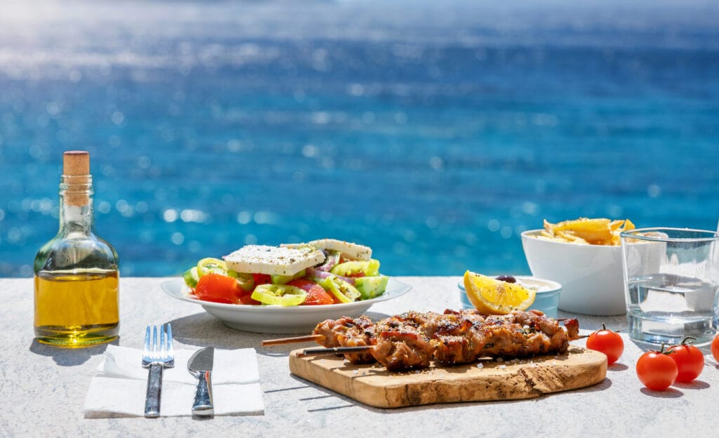 Souvlaki and greek salad in front of the sparkling blue Aegean sea.