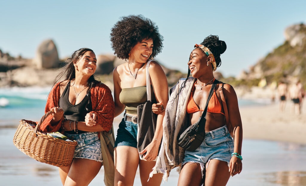 Shot of three friends arriving at the beach with a picnic basket.