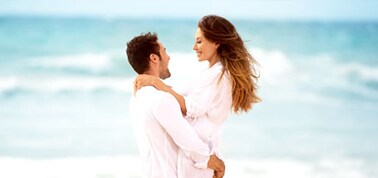 a couple dressed in white hugging on a beach